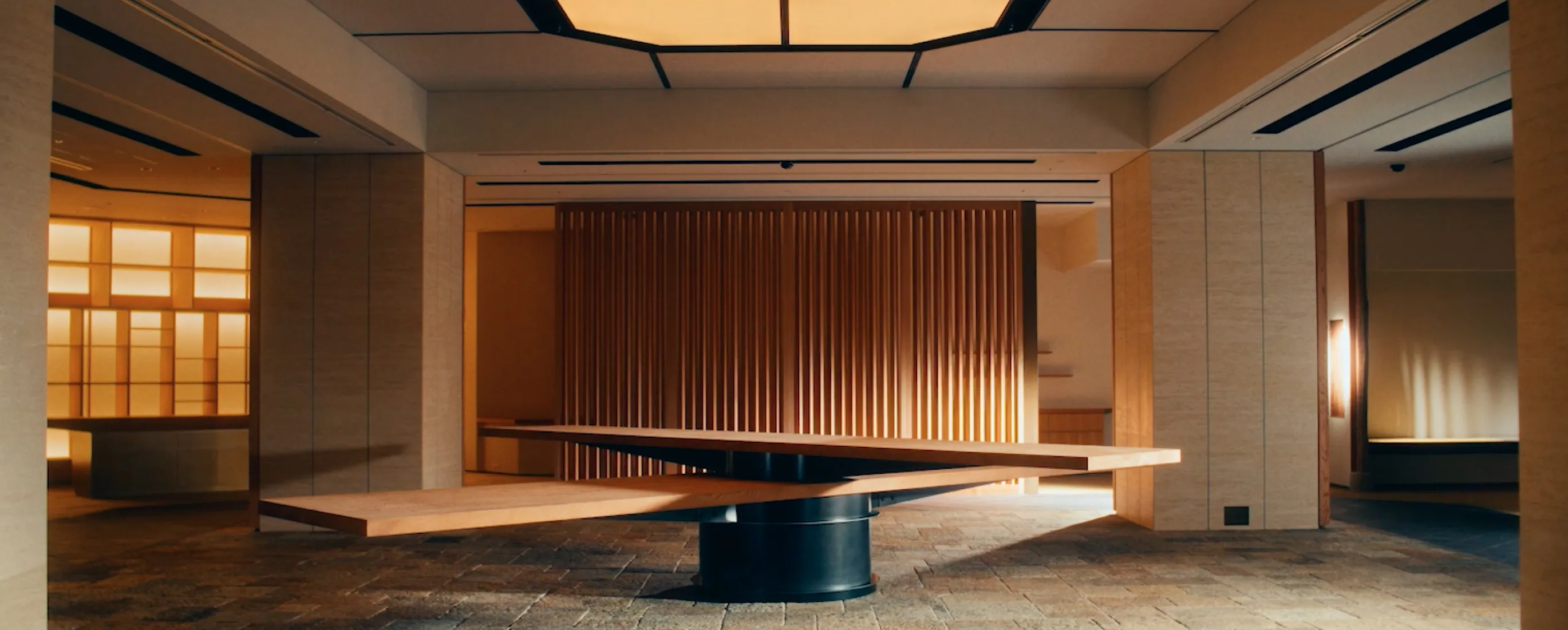 洗練された和モダンな内装の広々としたロビー。中央には特徴的な木製のデザインテーブルが配置され、石畳と木のぬくもりが調和している。